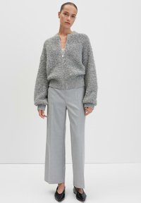 Grijze textured zip-up sweater met oversized mouwen, gecombineerd met lichtgrijze wijde broek en zwarte puntige flats.