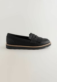Sorte læder slip-on sko med frynse detaljer, takkede kanter og en flad gummisål med en kontrasterende beige kant.