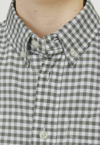 Camicia a quadri verde e bianco con colletto classico e bottoni in plastica, dotata di taschino sul lato sinistro.