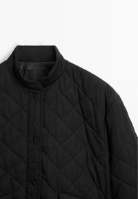 Giacca nera trapuntata con colletto alto, chiusura con bottoni a scatto e motivo a rombi orizzontali sul tessuto. Texture liscia, design leggero.