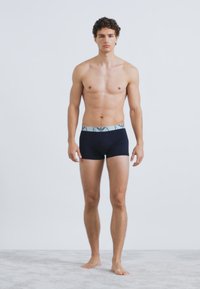 Tengerészkék színű férfi boxeralsó világoskék derékszalaggal, logó díszítéssel. Simább anyag, testhezálló szabás és lapos varrások a kényelemért.