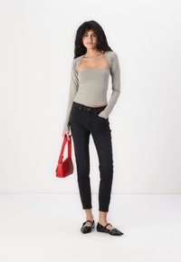 Ljusgrå långärmad topp, svarta slim jeans och svarta flats med ögla detaljer; håller en liten röd handväska. Enkel, modern passform.