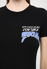 T-shirt in cotone nero con stampa grafica in bianco e blu che recita "Versace Jeans Couture Tour" nell'area del petto a sinistra.