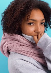 Pink knit scarf wrapped around a gray sweatshirt-clad shoulder, with textured patterns. Close-up of a face showing curly hair and a hand near the mouth.