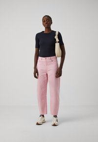Námornícky pruhovaný top s krátkym rukávom, svetloružové nohavice rovného strihu s prednými vreckami a béžová crossbody taška. Svetlé športové topánky s akcentmi.