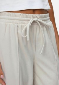 Pantalons côtelés beige clair avec une taille élastique et un cordon de serrage. Comprend des poches latérales et une coupe décontractée, avec une texture douce.