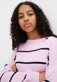 Maglione rosa chiaro con strisce orizzontali nere, polsini a coste e scollatura rotonda. Il tessuto sembra morbido e texture.