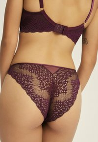 Lila Spitzenunterwäsche-Set mit einem detaillierten Netzdesign. Der BH hat verstellbare Träger und einen Hakenverschluss; der passende Tanga hat einen durchsichtigen Rücken.