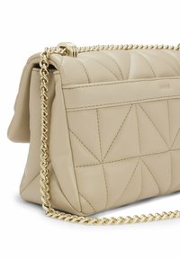 Beżowa pikowana skórzana torebka na ramię z złotym łańcuszkiem i charakterystycznym trójkątnym wzorem. Na przedniej stronie znajduje się subtelne logo wytłoczone w skórze.