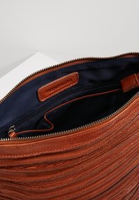 Hnědá kožená taška s texturovaným, nažehleným designem. Interiér má tmavou látkovou podšívku a zipovou kapsu pro uložení.