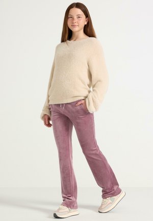 Pull beige duveteux à manches longues associé à un pantalon de survêtement rose pâle et des baskets claires, présentant une surface texturée et une taille élastique.