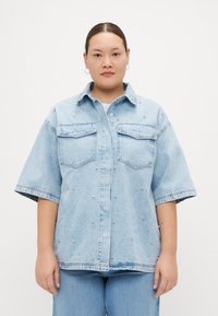 Lys blå denimskjorte med korte ermer, to brystlommer og s�ølvnitter som pynter framsiden. Uformell, løs passform.