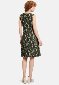 Ärmelloses Kleid mit tailliertem Oberteil und ausgestellt Rock. Es hat ein grün-schwarz abstraktes Muster und besteht aus leichtem Stoff.