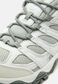 Gros plan d'une chaussure de randonnée grise et blanche avec tissu en mesh, overlays en suède, embout renforcé et lacets durables noués en motif croisé.