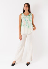 Blusa senza maniche con stampa floreale in morbido tessuto leggero dai toni verde e pesca, abbinata a pantaloni bianchi a gamba larga e décolleté neri a punta.