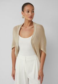 Beige gebreide cardigan met korte mouwen, open voorkant, gecombineerd met een wit tanktop en witte hoge taillebroek. Minimalistische stijl.