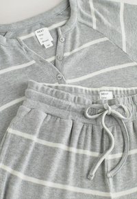 Set de pijama cu dungi gri, format dintr-un tricou henley cu pliere cu nasturi și pantaloni cu talie ajustabilă prin șnur. Material moale din bumbac cu dungi albe.