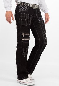 Pantaloni cargo in denim nero con molteplici tasche, cerniere e dettagli di cucitura bianca. Design aderente con gamba dritta e cintura.