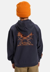 Navy hoodie with orange graphic on the back featuring abstract designs. Includes a drawstring hood and ribbed cuffs. Worn with an orange beanie.