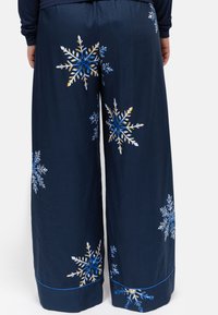 Pantalons de pyjama bleu marine à coupe décontractée, ornés de motifs de flocons de neige colorés. Matériel doux avec un accent bleu le long de l'ourlet.