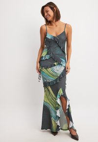 Long, fitted dress with spaghetti straps, featuring ruffled layers in shades of green and blue on a dark background, side slit, and white accents.
