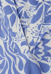 Gros plan d'un tissu bleu et blanc avec un imprimé floral abstrait et un col en V avec des détails de couture visibles.