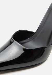 Μαύρο παπούτσι γόβα με μυτερή μύτη από δέρμα με γυαλιστερή, λεία επιφάνεια, παρουσιάζεται σε λευκό φόντο.