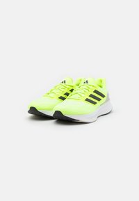 Zapatillas deportivas verde lima con rayas negras, parte superior de tejido de malla, diseño de cordones, suela acolchada y suela exterior de goma negra texturizada.
