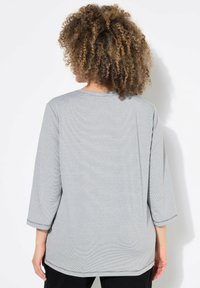 Maglietta a maniche lunghe grigia chiara con una vestibilità rilassata, texture a coste, scollatura rotonda e dettagli di cuciture nere. La vista mostra il retro.