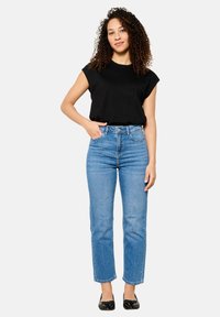 Top negro de algodón de manga corta combinado con jeans rectos de tiro alto y largos recortados en azul claro, usados con planos negros.