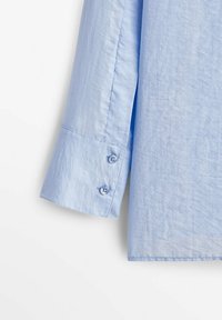 Jasnoniebieska koszula z długim rękawem i mankietem na guziki, wykonana z miękkiego materiału. Charakteryzuje się gładką fakturą i starannym wykończeniem na dole.