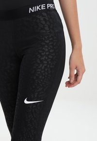 Černé legíny Nike Pro s texturovaným leopardím potiskem a bílým logem na dolní části nohavic, s širokým elastickým pasem.