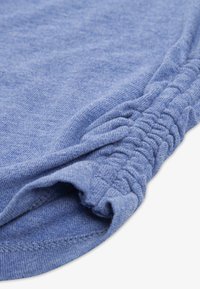 Svetlo modra bombažna tkanina z mehko teksturo, ki ima naborke ob robu in gladko, rahlo ukrivljen rob.