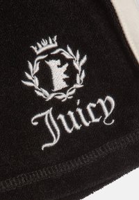 Μαύρο υφαντό ύφασμα με λευκό κεντημένο έμβλημα αρκούδας με στέμμα και καλλιγραφική επιγραφή "Juicy" από κάτω.