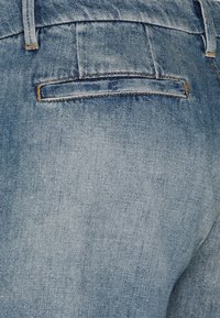 Jeans de mezclilla de color azul claro con un acabado texturizado, que cuentan con un bolsillo trasero y detalles de costura amarilla. Diseño sencillo con un corte clásico.