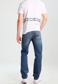 Vit t-shirt med svart Reebok-logoband, parat med blå jeans. Jeanserna har en blekt finish och två bakfickor. Vita sneakers.