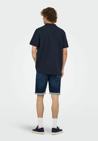 Navy polo shirt, short sleeves, worn with rolled denim shorts, featuring a faded wash, white socks, and dark sneakers.