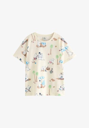 Ung pige står smilende iført en cremefarvet T-shirt med tegneseriefigurer, hvide shorts, blå sokker, hvide sneakers og farverige perlesmykker.
