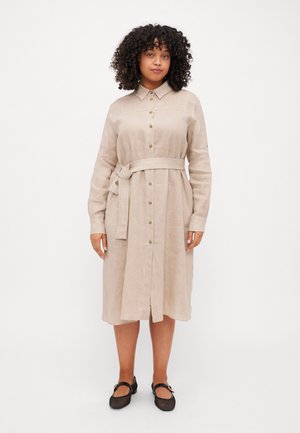Robe chemise en lin beige avec col, boutons sur le devant, manches longues et ceinture en tissu. Présente une coupe mi-genoux et de légers fentes sur les côtés.