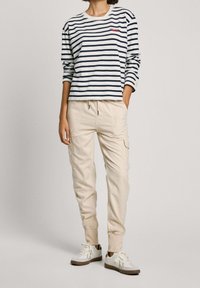 Striped long-sleeve shirt in navy and white, paired with light beige cargo pants and white sneakers with brown accents.