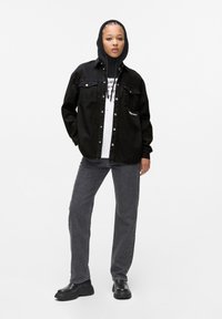 Black denim jacket with snap buttons, paired with a white graphic t-shirt, gray denim jeans, and black chunky boots. Textured fabric and hood.