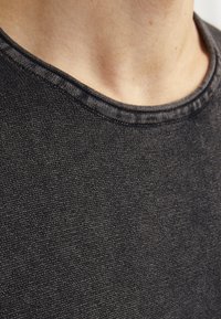 Nærbilde av svart stoff på en crew neck t-skjorte med teksturert veving og synlig søm langs kragen.