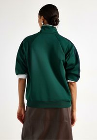 Grøn sweatshirt med høj krave, oversized pasform og korte ærmer. Har ribbet kant og kontrastfarvede mørke sidestriber.