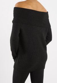 Černý svetr bez ramínek s žebrovaným výstřihem a dlouhými rukávy. Pletená textura s volným střihem, končící v oblasti boků, bez viditelných vzorů.