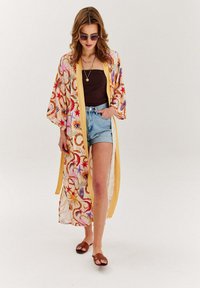 Lehký a vzdušný kimono s jasnými květinovými a okatými vzory, žlutými lemy a rukávy po třičtvrtě, v kombinaci s denimovými kraťasy a sandály.