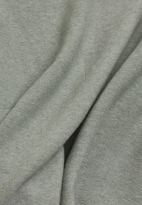 Tissu texturé gris drapé, montrant un motif de tricot serré avec une légère brillance. La surface semble lisse et uniforme, créant de douces plis.