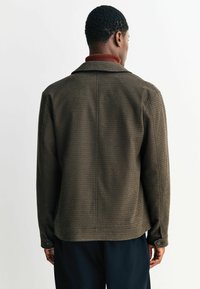 Braun kariertes Jackett mit einem taillierten Kragen, Knopfmanschetten und einer lockeren Passform, das aus einem strukturierten gewebten Stoff besteht und subtile Nahtdetails aufweist.