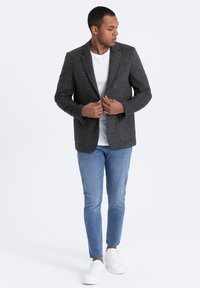 Schwarze und graue karierte Jacke mit Revers, kombiniert mit einem weißen T-Shirt, hellblauen Jeans und weißen Sneakern.