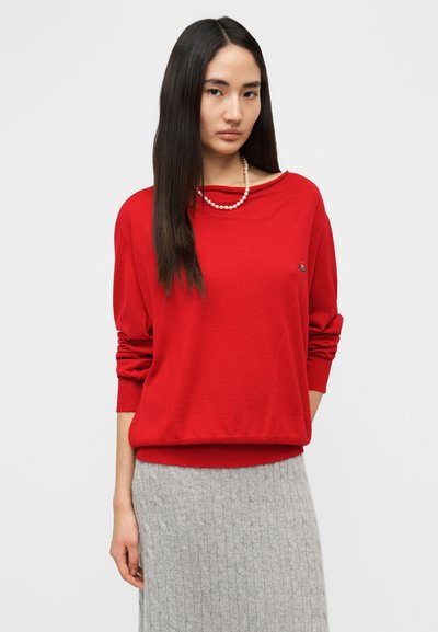 Κόκκινο πλεκτό πουλόβερ με άνετη εφαρμογή, λαιμόκοψη σε σχήμα βάρκας και μακριά μανίκια. Διαθέτει ριμπ μανσέτες και τελείωμα. Συνδυάζεται με φούστα σε ανοιχτό γκρι με υφή.