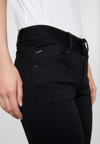 Černé džínové kalhoty s obepínajícím střihem, kontrastním prošíváním, standardními kapsami a označením značky na pasu.